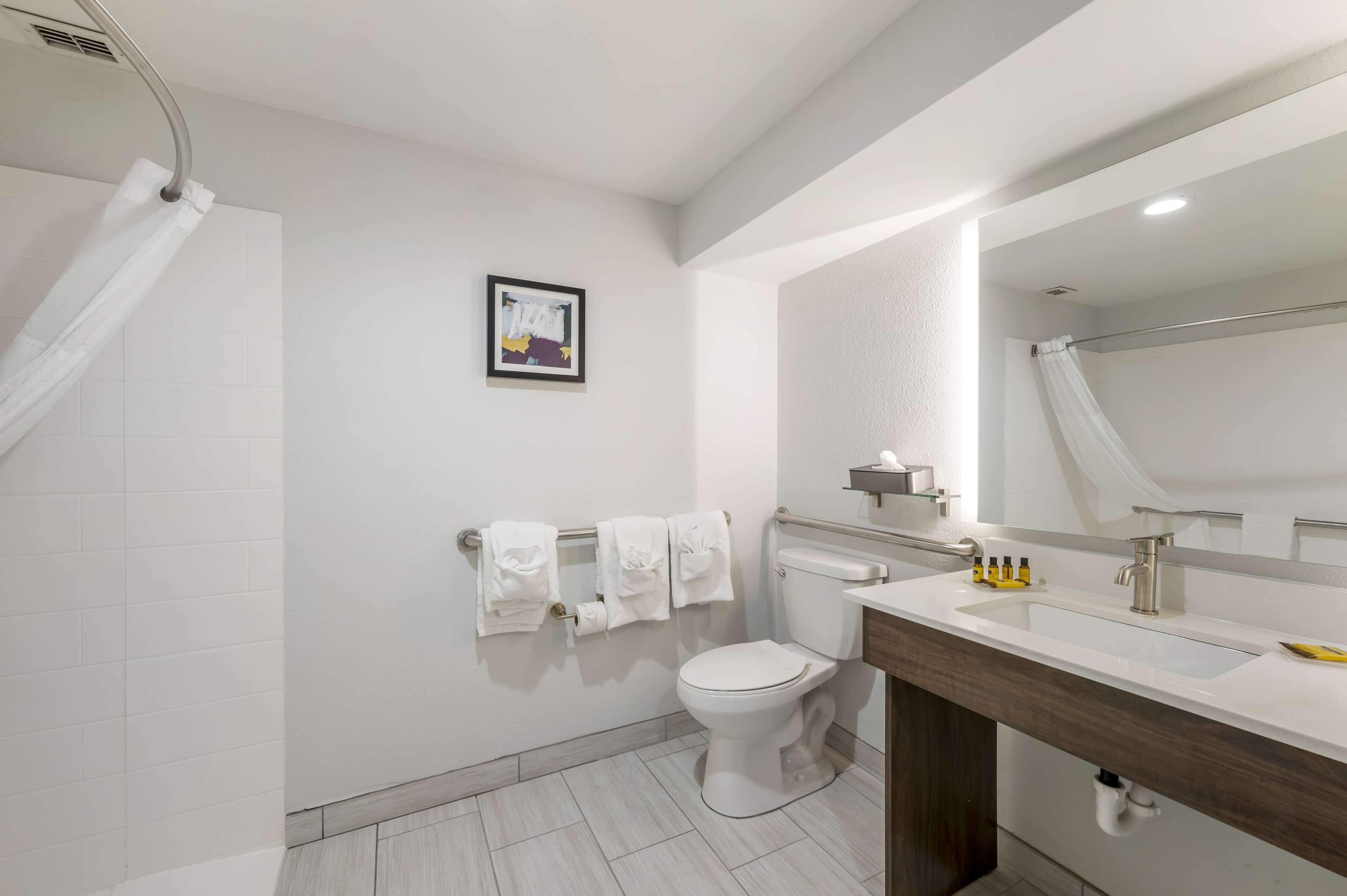 A modern bathroom with a toilet, sink, and shower area. There is a framed picture on the wall and towels hanging on a rack.