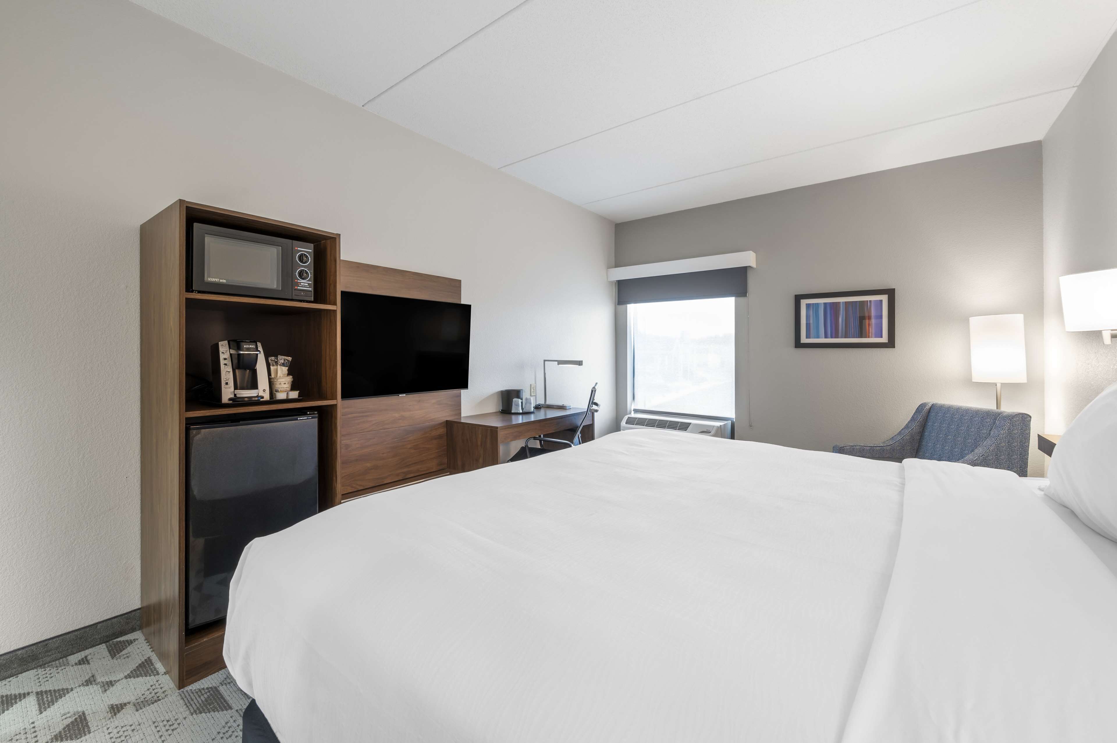 A hotel room with a large bed, a desk with a computer, a microwave, and a refrigerator.