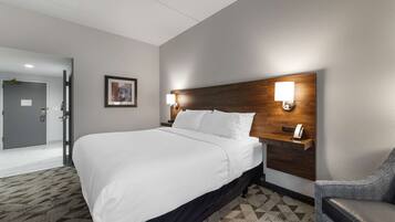 A hotel room with a large bed, a wooden headboard, two bedside lamps, a desk with a phone, and a patterned carpet.