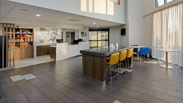 A modern kitchen with a central island, bar seating, and a dining area with blue chairs. - Best Western Plus Harrisonburg (Harrisonburg)