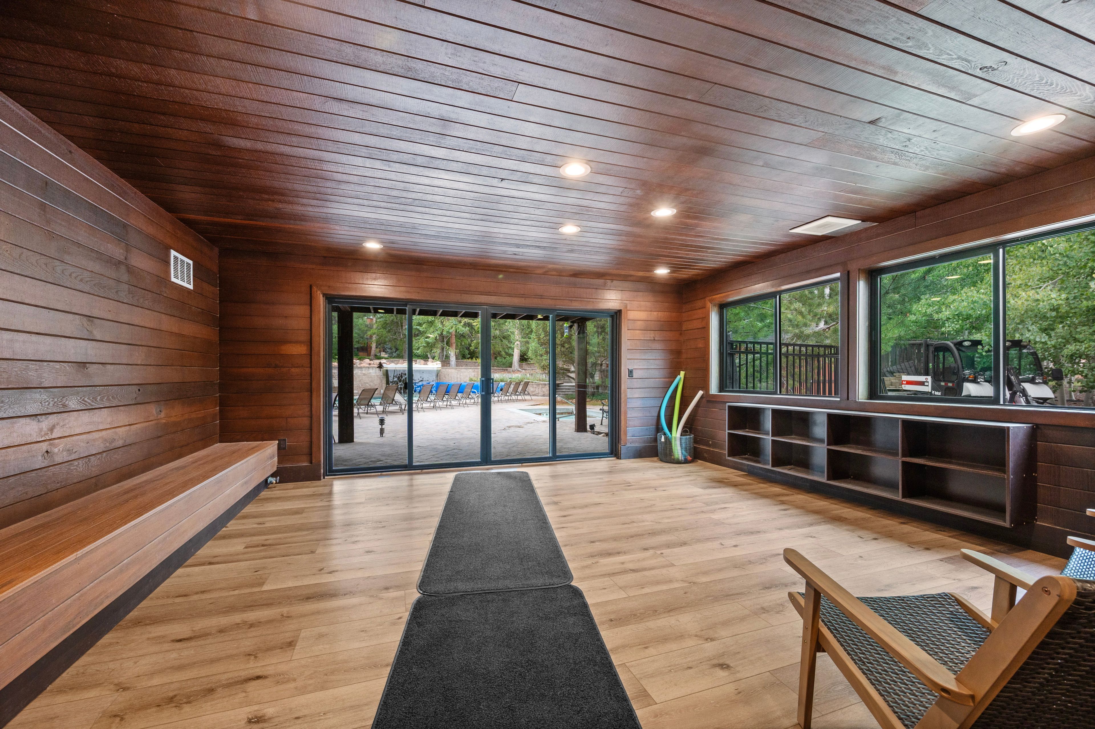 A wooden interior with a bench, a door leading outside, and a view of the outdoors.