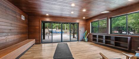 A wooden interior with a bench, a door leading outside, and a view of the outdoors.