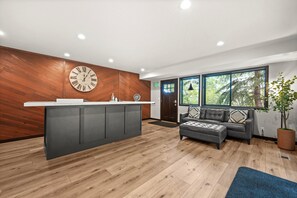 Un espace d’accueil avec un mur en bois, une horloge, un comptoir de réception, un canapé et une grande fenêtre donnant sur des arbres.
