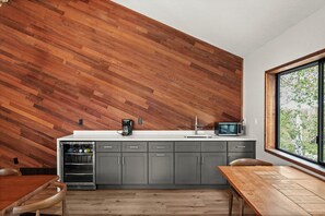 Une cuisine moderne avec un mur en bois disposé en motif chevron, un four à micro-ondes encastré et une fenêtre donnant sur la verdure.
