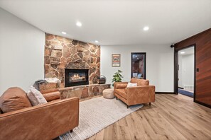A modern living room with a stone fireplace, leather sofas, and a wooden floor.