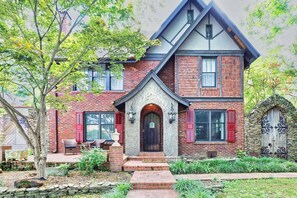 A two-story house with a stone facade, a prominent front door, and a small porch with outdoor seating. - Heated Pool-Historic Tudor Home-Crestmere Estate (Memphis)