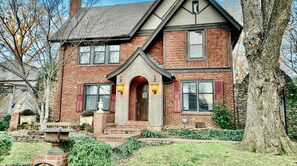 A two-story brick house with a gabled roof, a front entrance with a small porch, and a stone wall with a decorative planter. - Heated Pool-Historic Tudor Home-Crestmere Estate (Memphis)