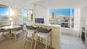 Una cocina moderna con una isla grande, un comedor con una mesa redonda y sillas, y ventanas amplias con vista a la ciudad.