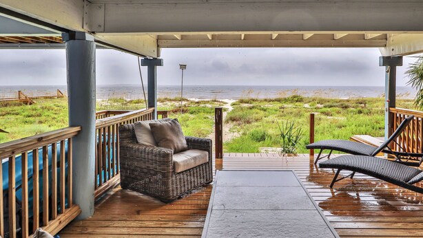 A covered outdoor area with wicker furniture and a view of the beach.