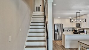 A modern kitchen with a central island, stainless steel appliances, and a staircase leading to another level.