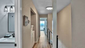 A hallway with wooden flooring, a white door, a white wall, and a view of the ocean through an open door.