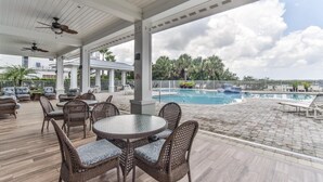 Un patio al aire libre con mobiliario de mimbre, una piscina y vistas a palmeras.