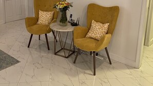 A room with two mustard-colored armchairs, a small round table with a vase of flowers, and a white door in the background. - Sapphire Villa Near the Sea-Entire Home (Nassau)