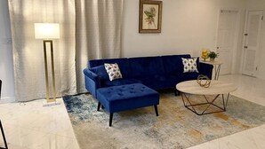 A living room with a blue sofa, a round coffee table, a floor lamp, and a painting on the wall. - Sapphire Villa Near the Sea-Entire Home (Nassau)