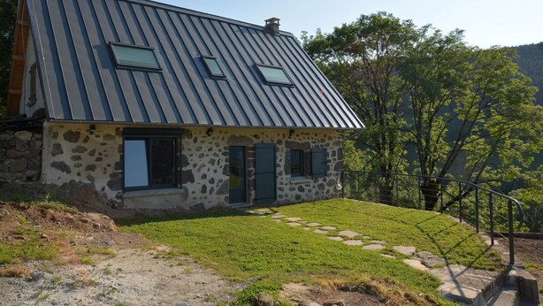 Una casa de piedra con techo metálico inclinado y un pequeño porche delantero.