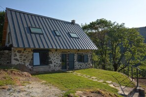 A stone house with a sloped metal roof and a small front porch. - Maison en pierre, au calme, terrasse en pelouse avec vue (Thiézac)