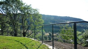 Barandilla de metal con vistas a una zona verde con árboles y un paisaje montañoso al fondo.