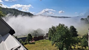 Vista desde una ventana hacia un valle brumoso, con cielo despejado y algunas nubes.