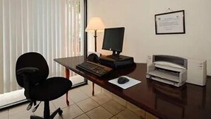 Un bureau d’hôtel équipé d’un bureau, d’un ordinateur, d’une imprimante, d’une chaise et d’une fenêtre avec des stores.