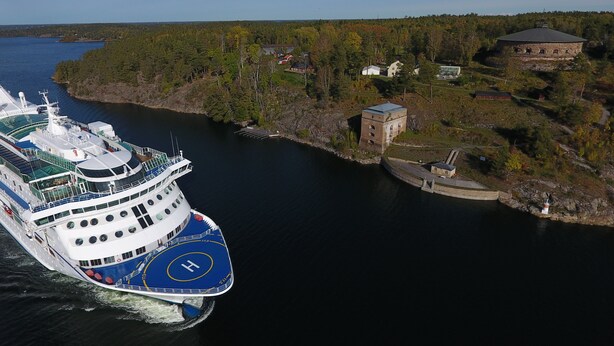 A cruise ship docked near a small island with a lighthouse and a stone building.