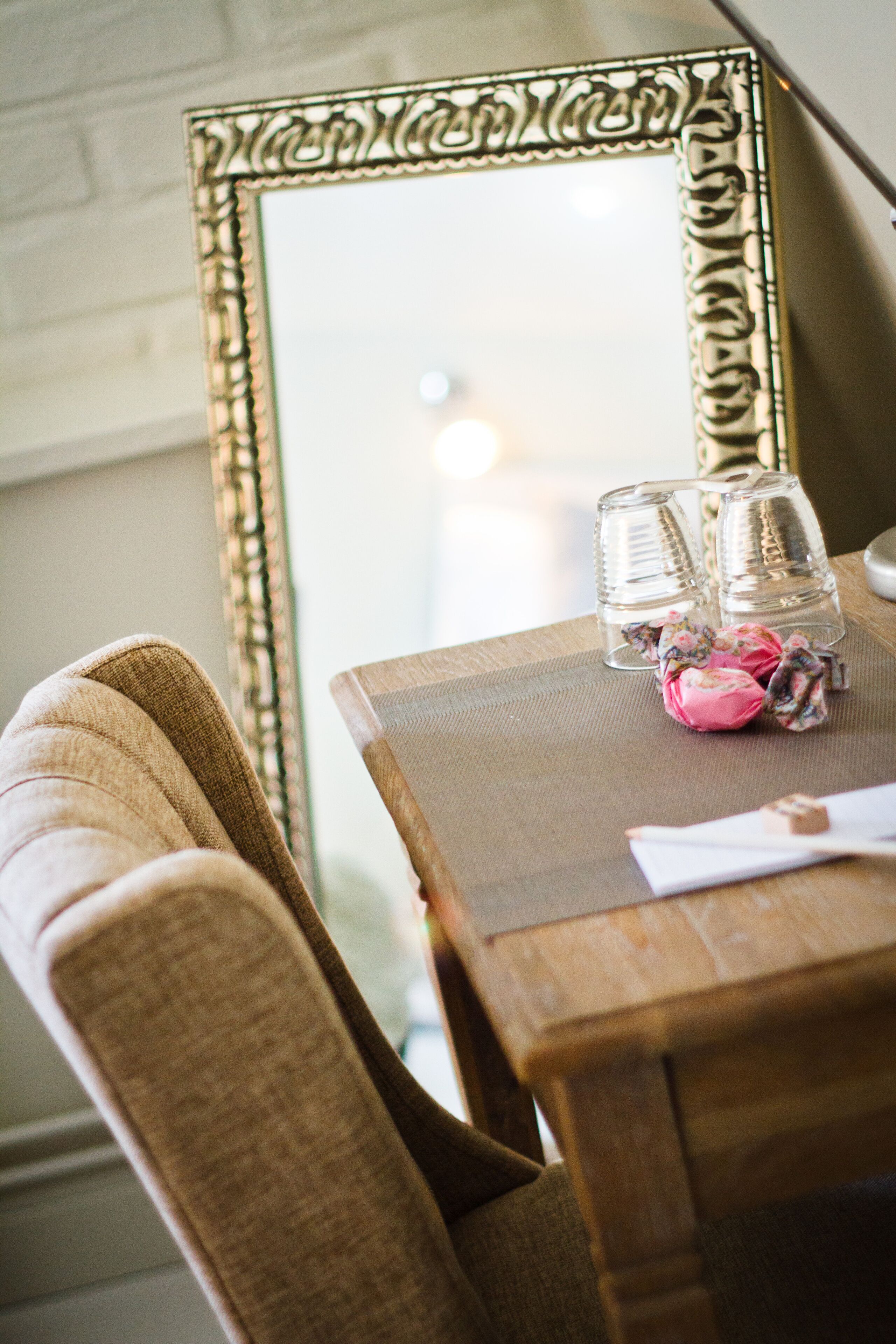 A wooden table with a mirror, two glasses, and a pink decorative item.