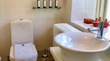 Une salle de bain équipée de toilettes, d’un lavabo, d’un radiateur et d’une étagère contenant des articles de toilette.