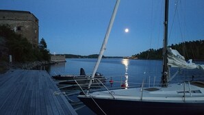 A wooden dock with boats moored alongside, a stone building on the left, and a calm body of water reflecting the moonlight. - Fredriksborg Hotel (Värmdö)