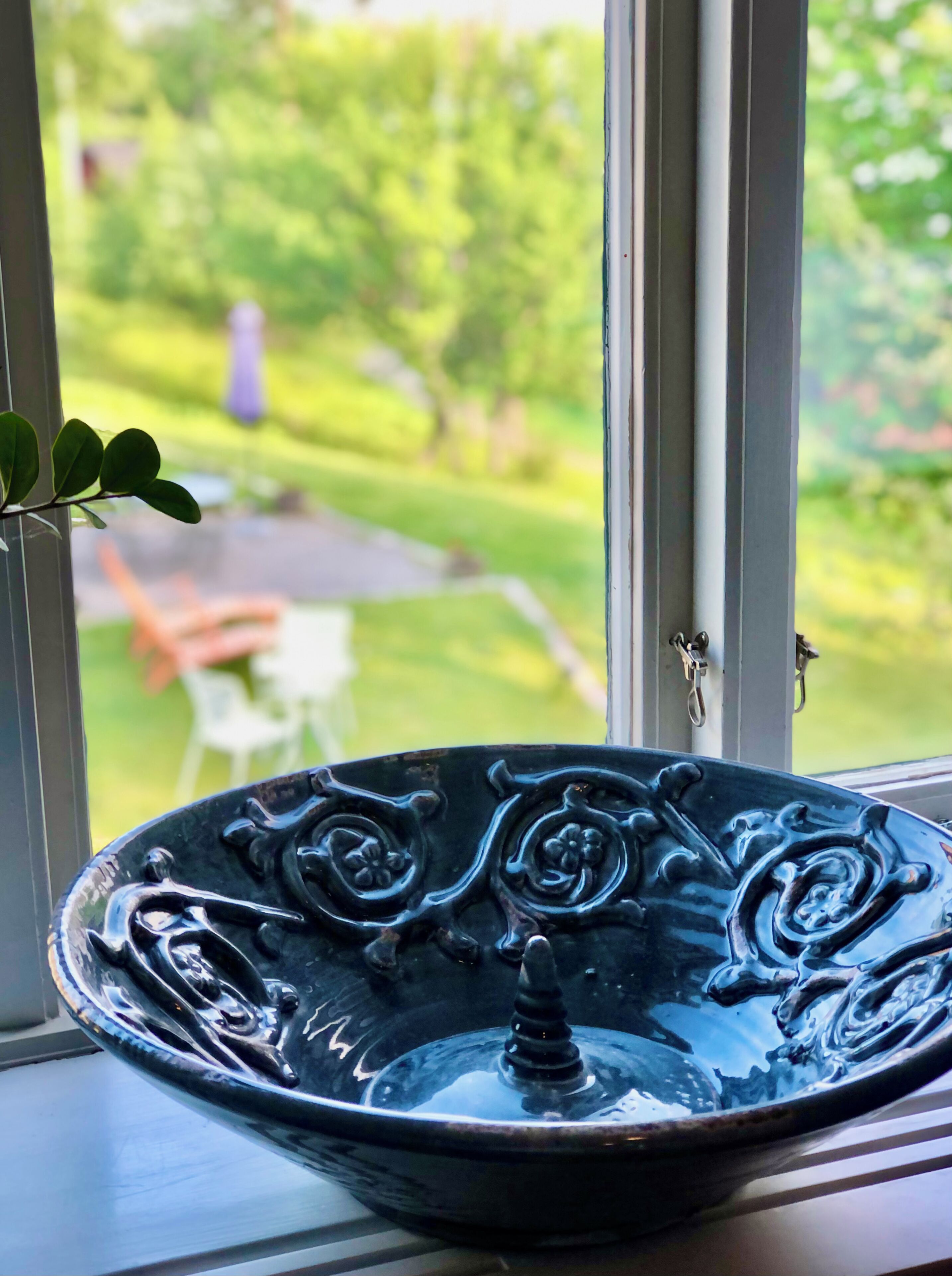 A black decorative bowl on a windowsill with a view of a garden and outdoor furniture.