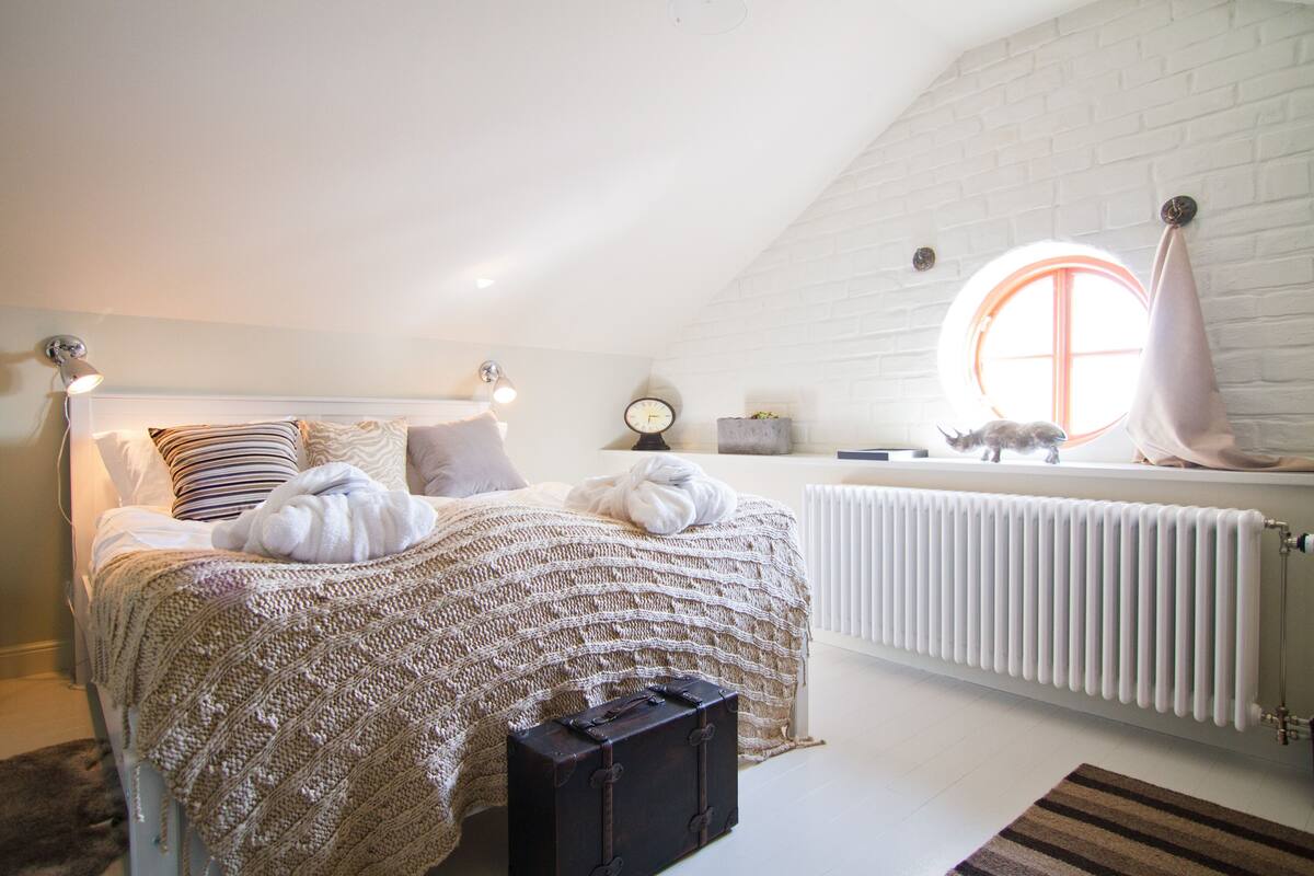 A cozy bedroom with a bed, a window, a radiator, and a suitcase.