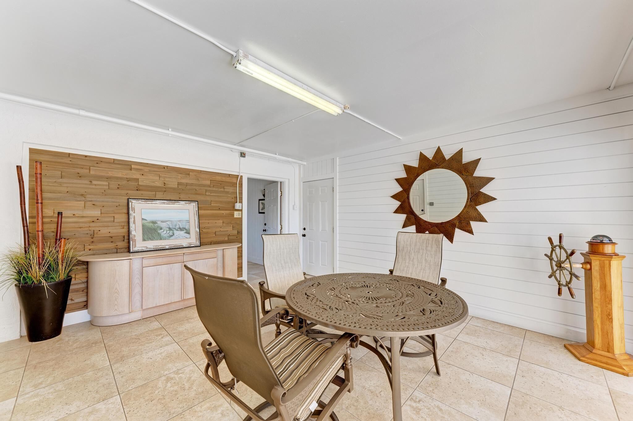 A sun-shaped mirror, a wooden cabinet, and a round table with chairs in a room with white walls and a tiled floor.