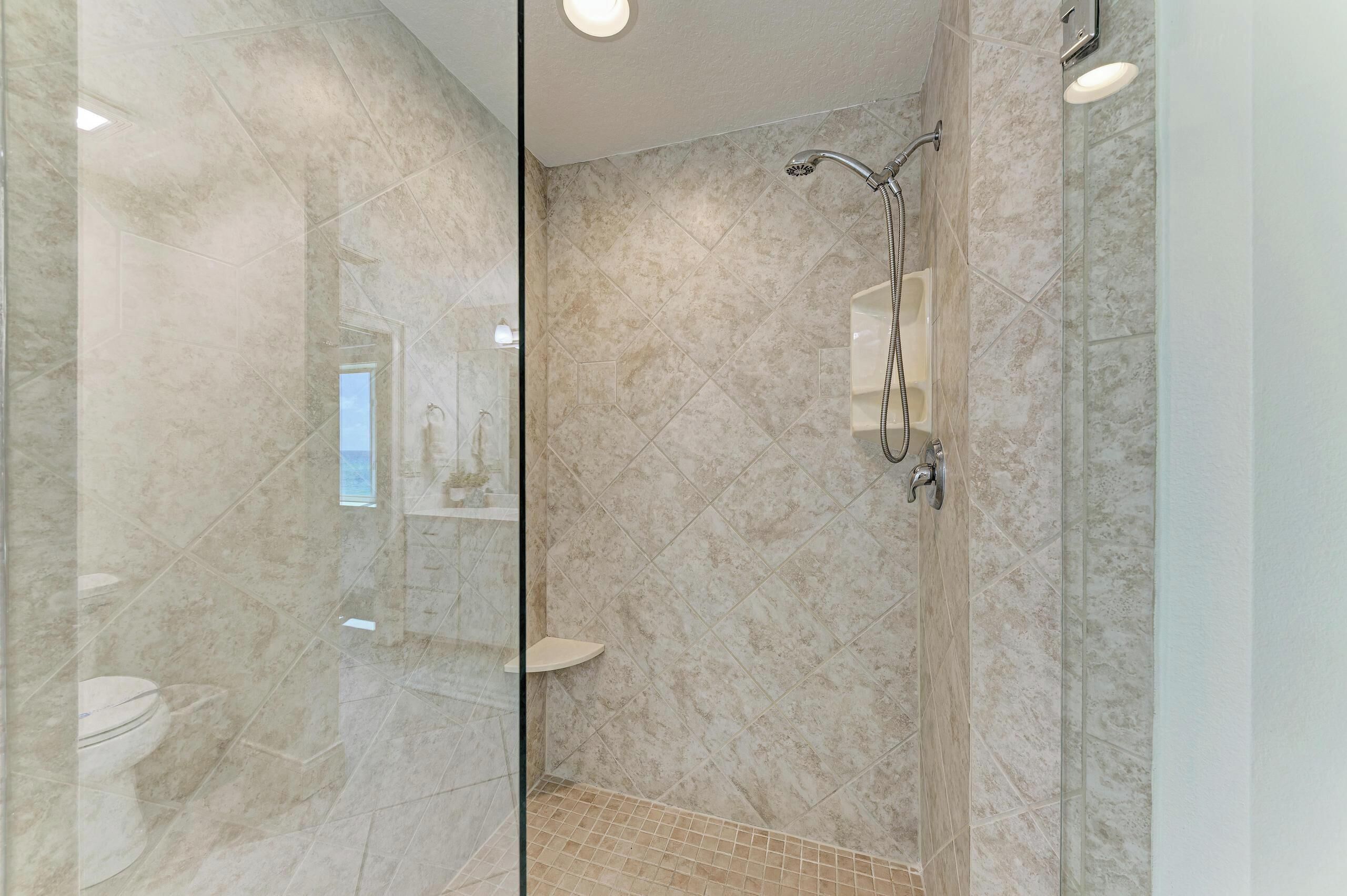 A modern bathroom with a glass-enclosed shower, marble tiles, and a visible toilet.