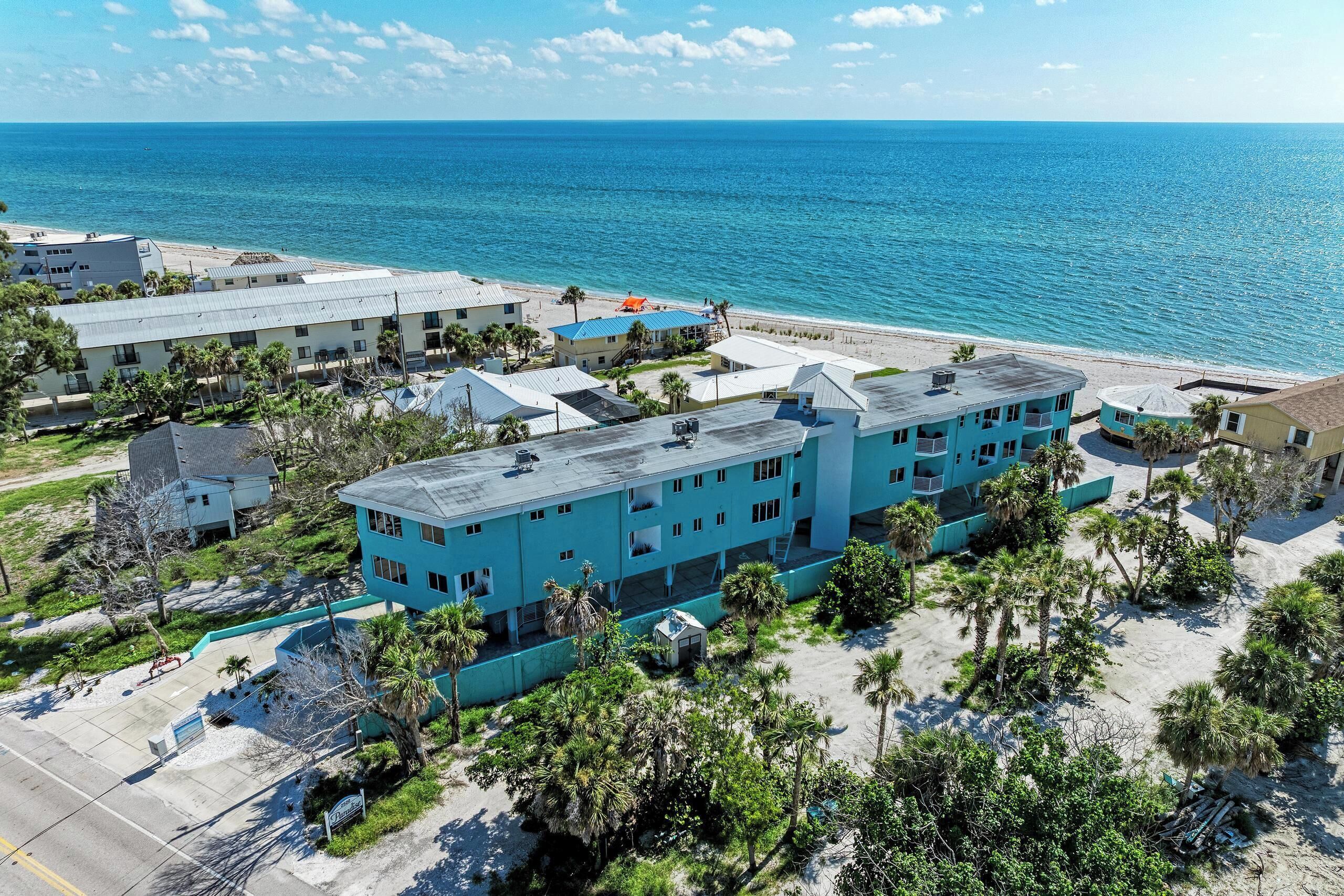 Un hotel junto a la costa con varias construcciones, vista a la playa y palmeras.