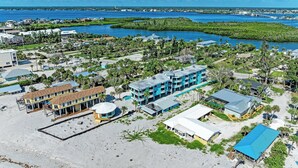 Vue aérienne d’un hôtel situé sur la côte, composé de plusieurs bâtiments, avec une plage et un port de plaisance.