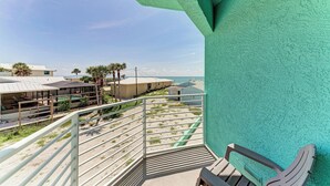 Un balcon avec vue sur la plage et les palmiers, un banc en bois et un mur turquoise.