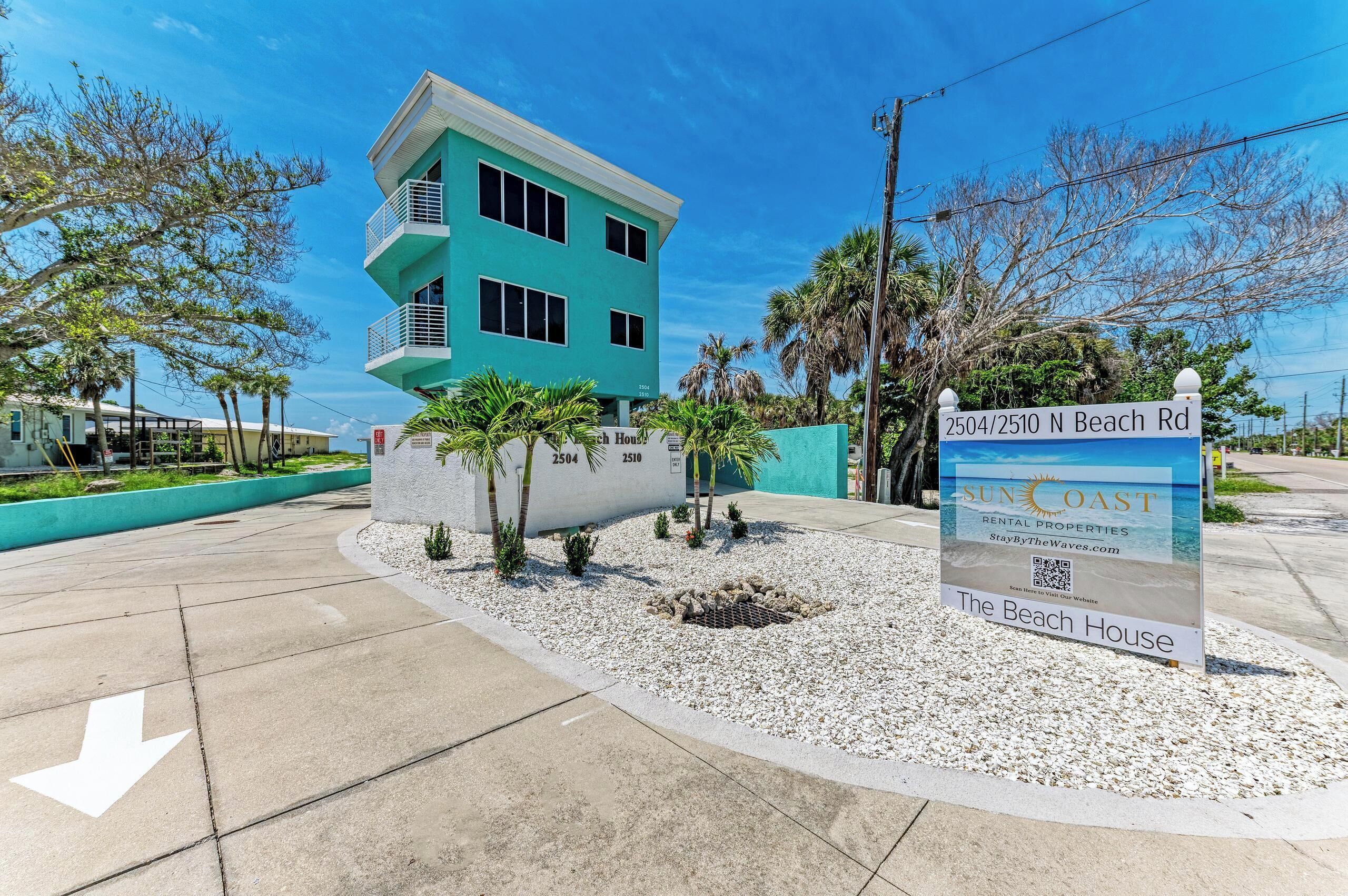 Un edificio de dos pisos con un balcón, un cartel que dice 'Sun Coast Rental Properties' y un letrero de casa de playa.