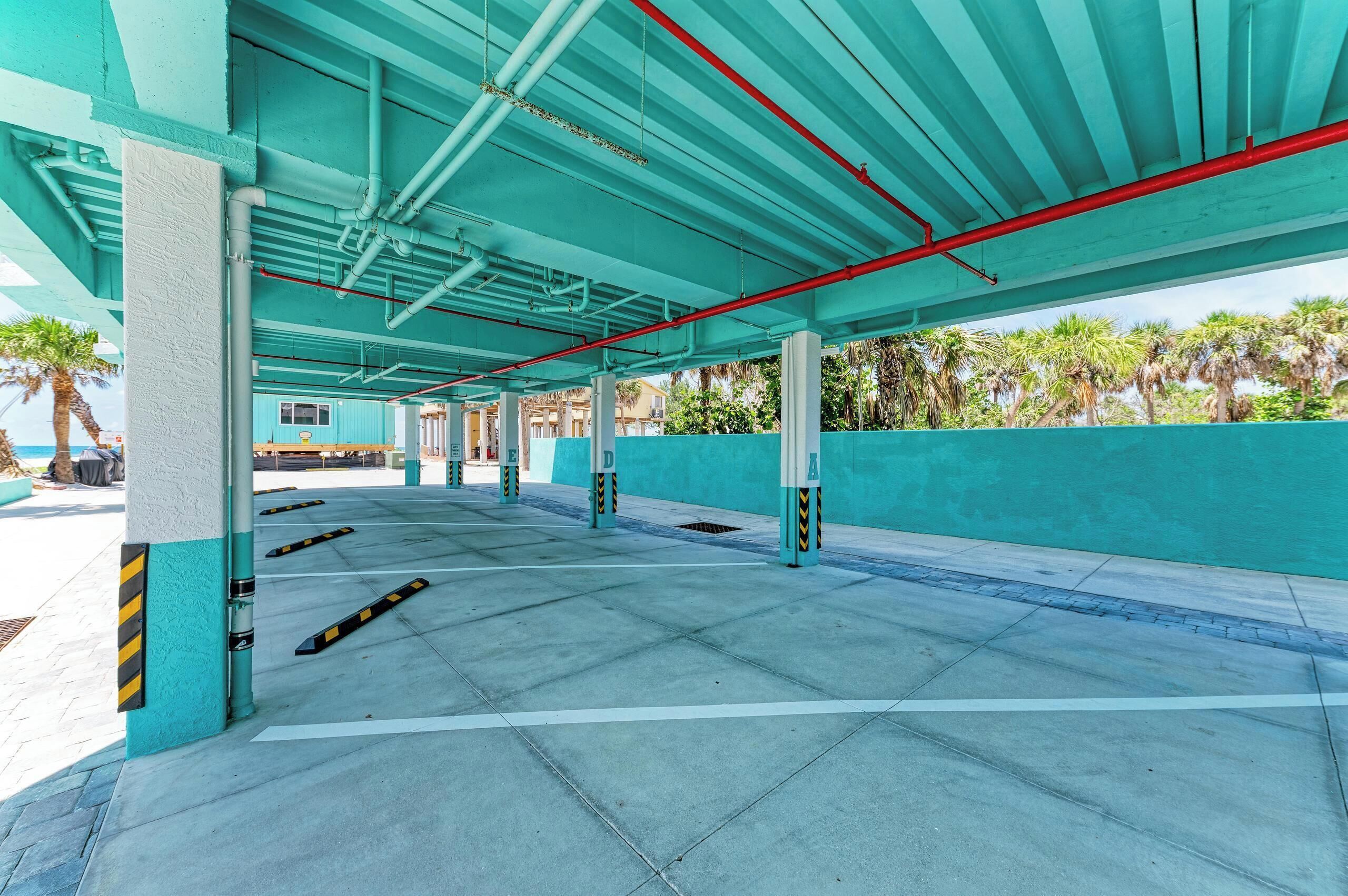 An empty parking garage with teal walls and columns, clear pathways, and a view of palm trees outside.