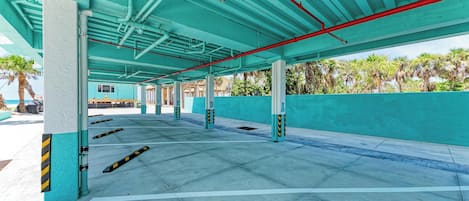 An empty parking garage with teal walls and columns, clear pathways, and a view of palm trees outside.