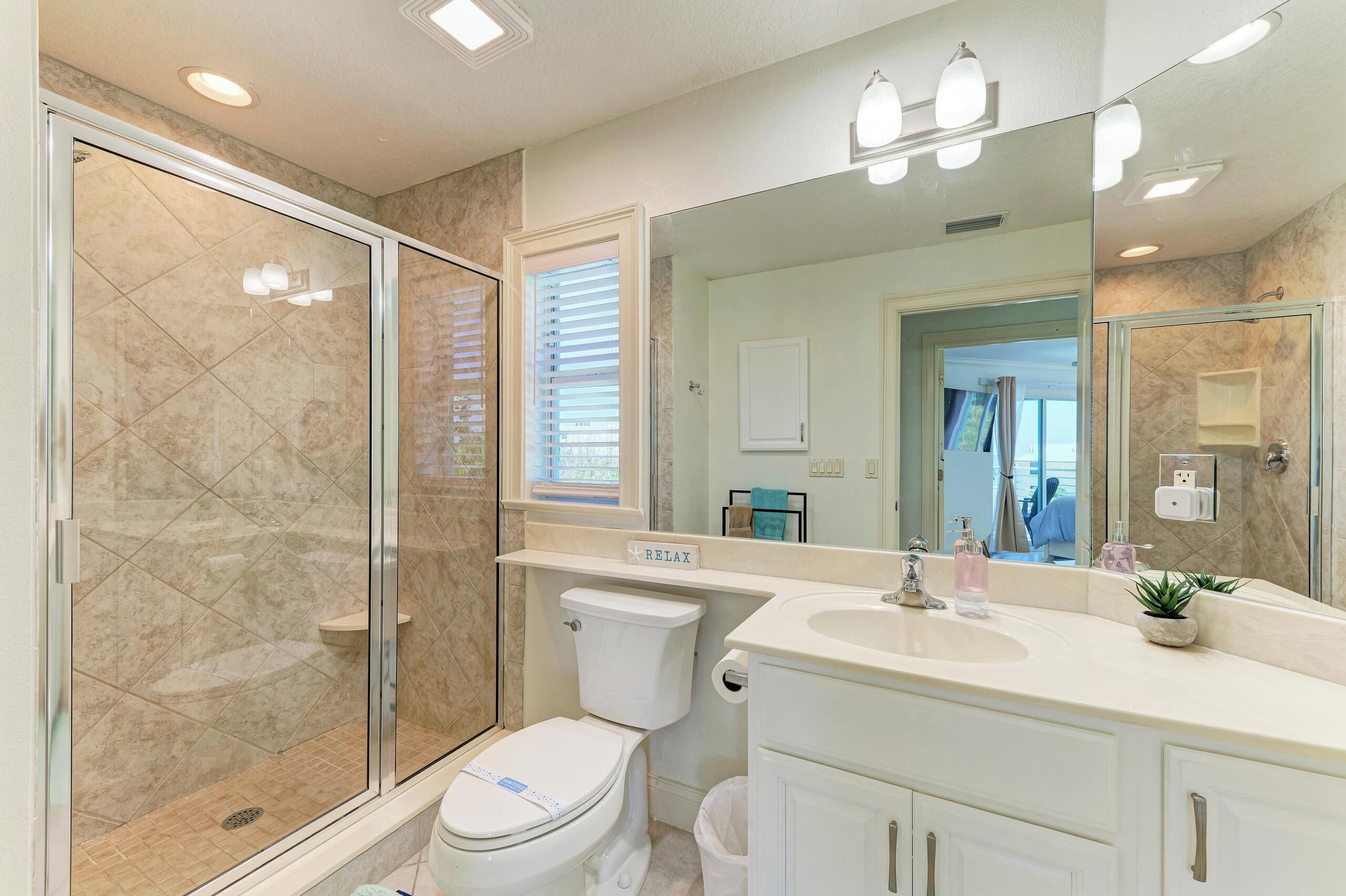 Une salle de bain avec une douche à parois de verre, des toilettes, un lavabo et un grand miroir.