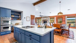A spacious kitchen with blue cabinets, a large island, and a dining area with wooden chairs and a view of the outdoors. - River l Resort Pool l Lake l Firepit l HOT TUB (Ingram)