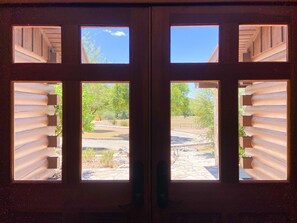 A set of wooden doors with multiple windows, each revealing a view of a landscaped outdoor area with trees and a stone pathway.