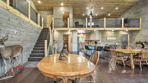 Un'ampia zona pranzo con un grande tavolo in legno e sedie, una scala che conduce al secondo piano e un angolo cottura visibile sullo sfondo.