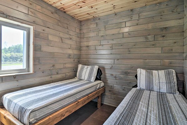 A cabin with two wooden beds, a window, and a view of greenery outside.