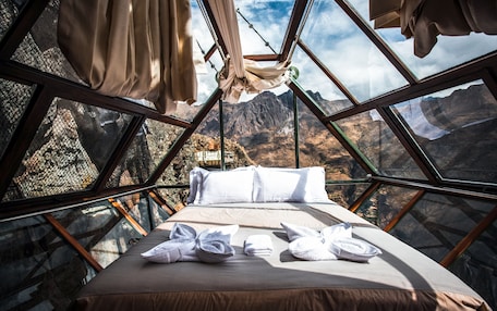 A bed with white linens and towels, a window with a mountain view, and a hanging hammock.