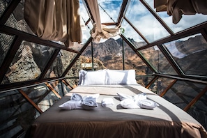 Una cama con sábanas y toallas blancas, una ventana con vista a las montañas y una hamaca colgante.