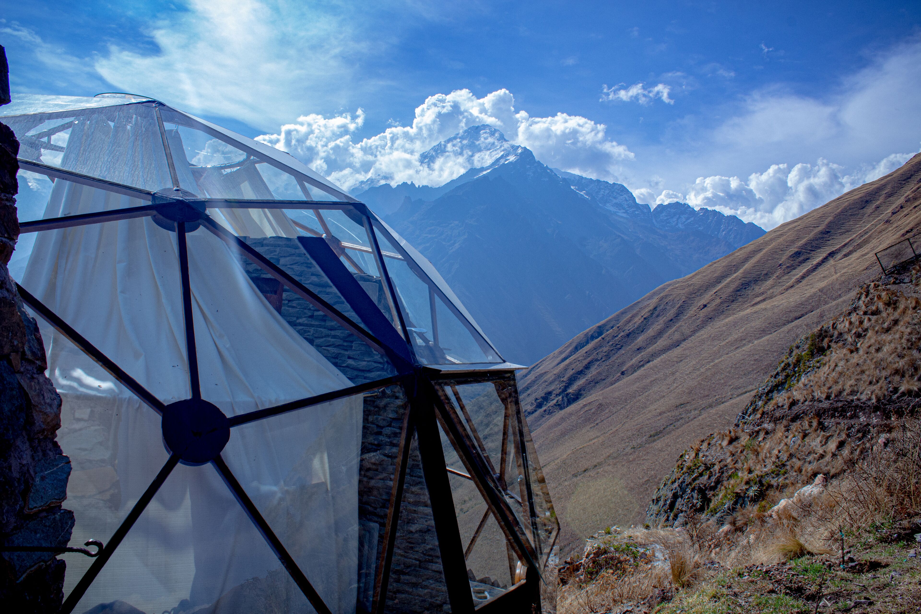 Une structure en forme de dôme géodésique, dotée d’une section transparente, se dressant sur un fond de paysage montagneux.