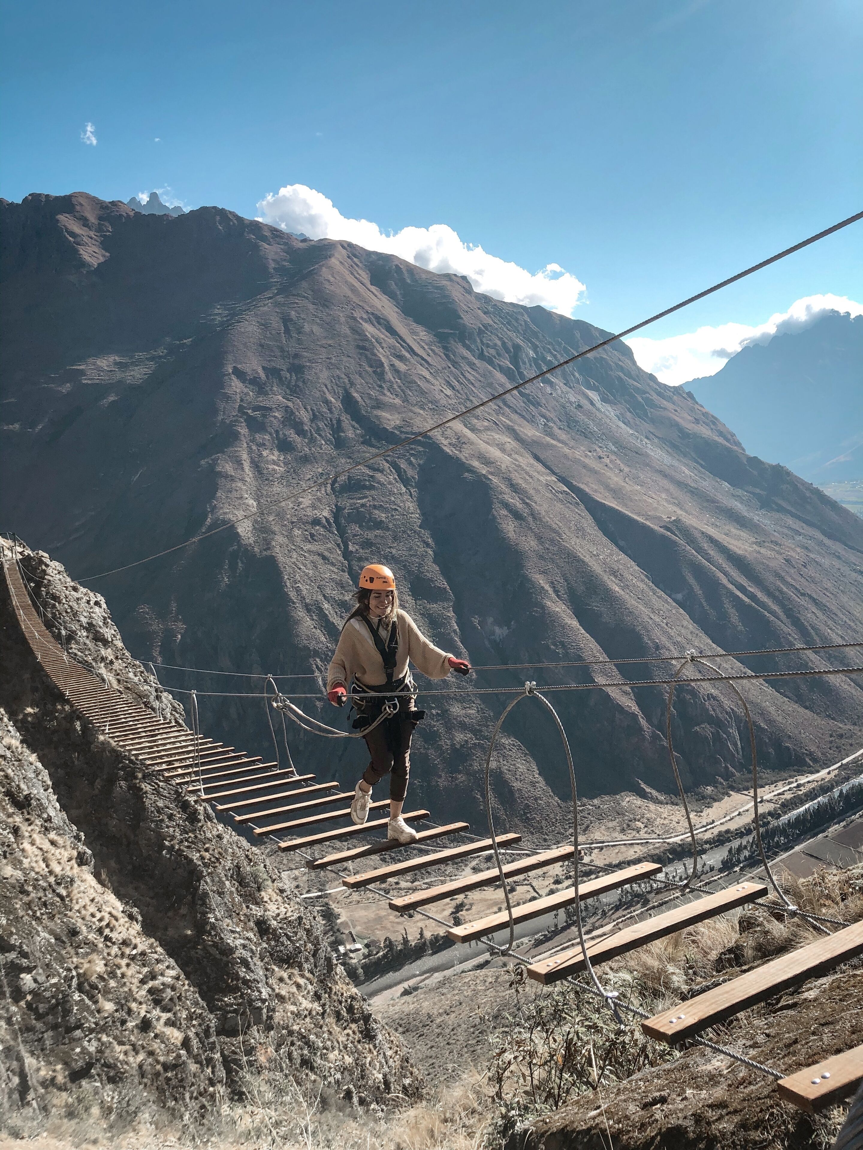 A person on a suspension bridge with a mountainous landscape in the background.