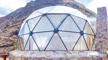 A geodesic dome structure with a stone base, set against a mountainous backdrop.