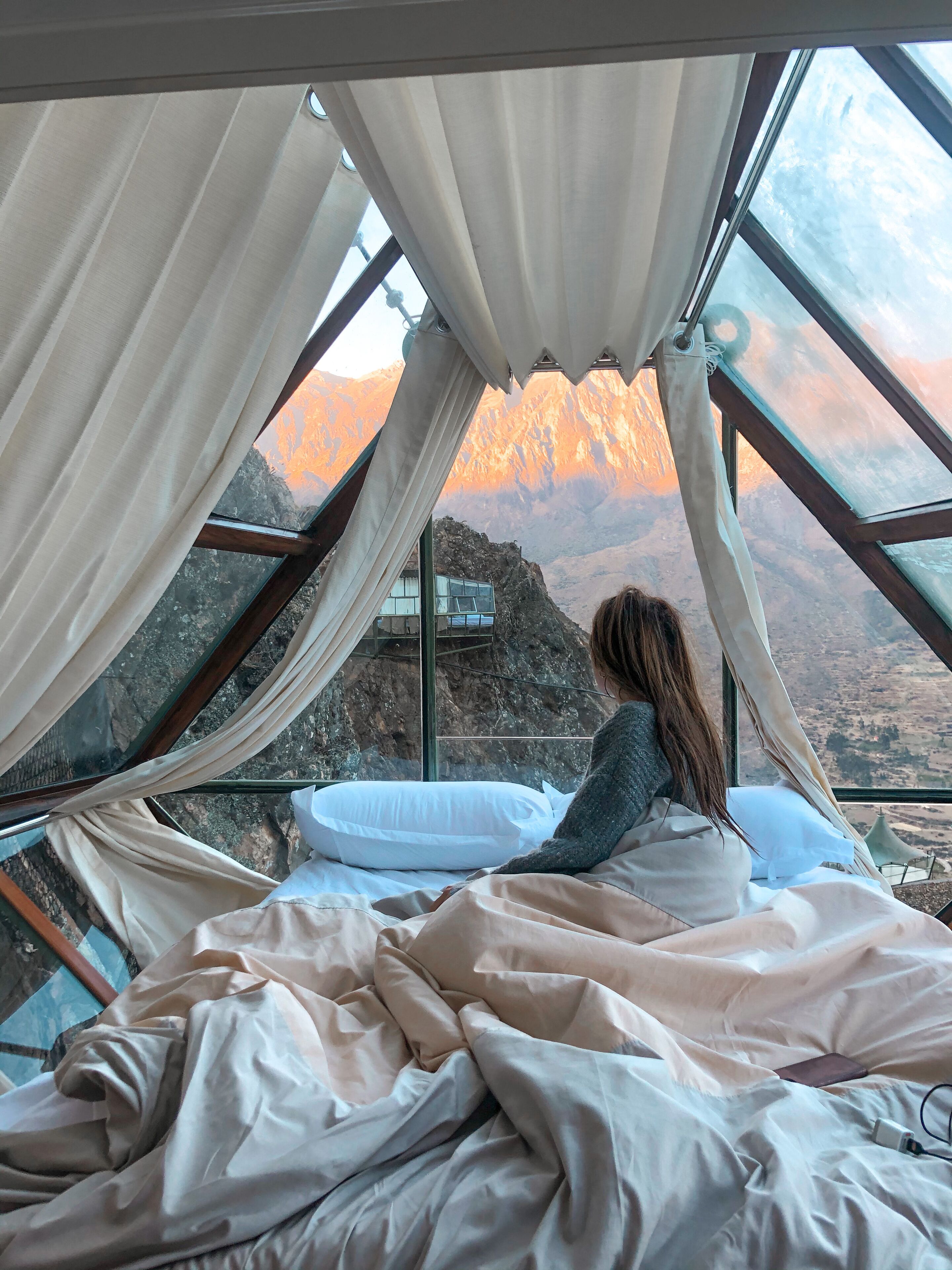 Una cama con vistas a una cadena montañosa a través de un techo de cristal.