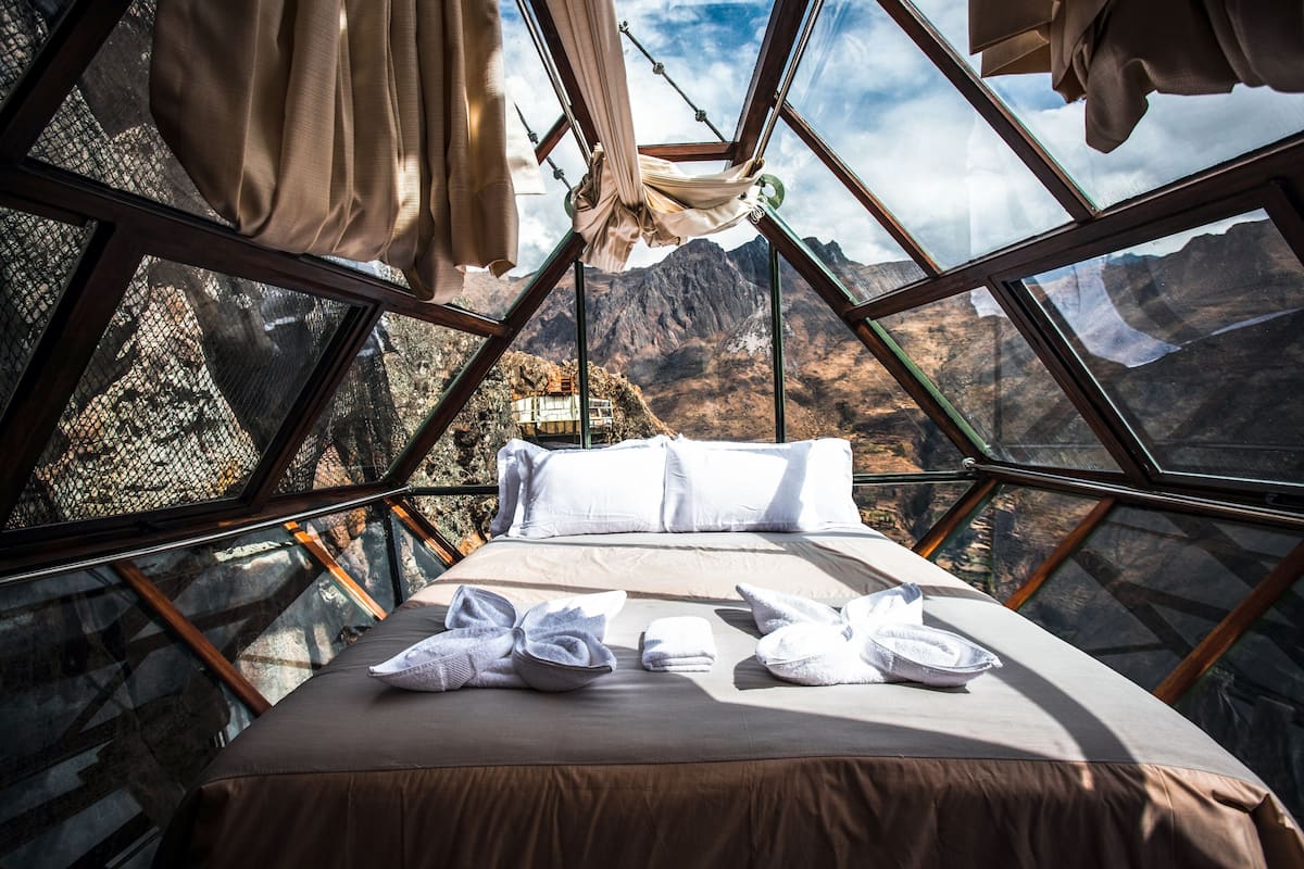 A room with a bed, towels, and a view of mountains through large windows.