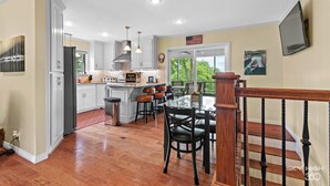 A spacious kitchen with white cabinets, a central island with stools, and a dining area with a wooden railing.
